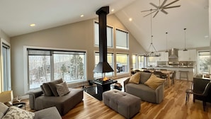 A spacious living area with a fireplace, large windows, and a modern kitchen. - Ski & relax with a view of the river - L'Aube Charlevoix (Petite-Rivière-Saint-François)