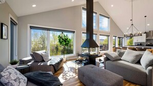 A modern living room with a fireplace, large windows, and a dining area. - Ski & relax with a view of the river - L'Aube Charlevoix (Petite-Rivière-Saint-François)