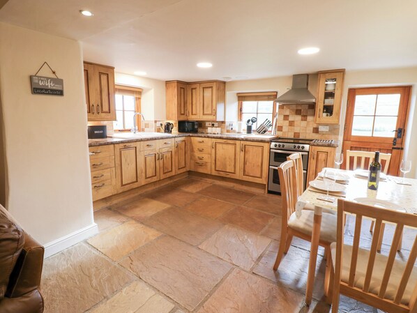 A spacious kitchen with wooden cabinets, a granite countertop, and a dining area with a table set for two. - Nick Jone (Richmond)