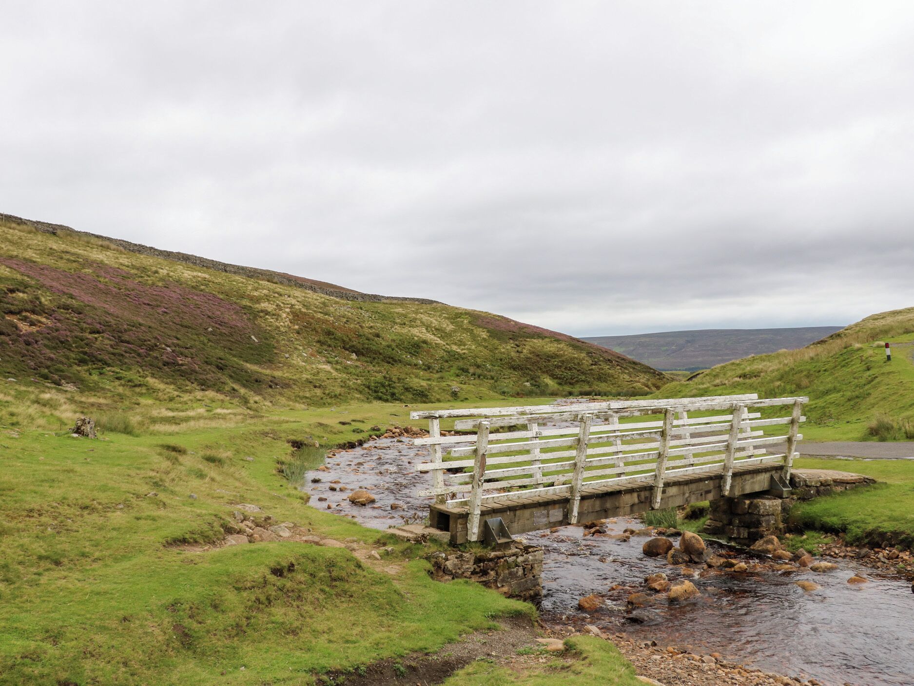A wooden bridge over a stream in a hilly landscape.