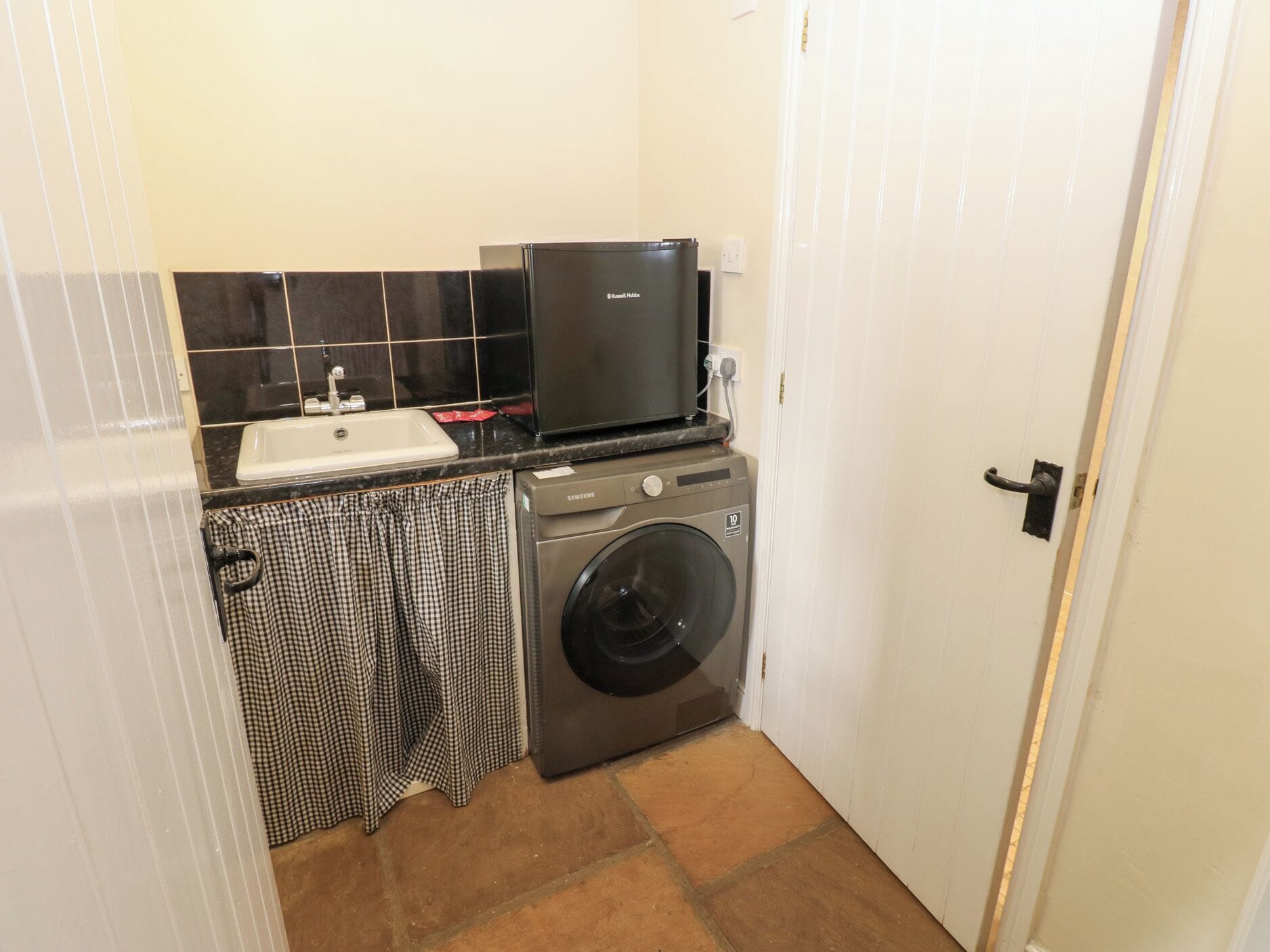 A compact laundry room with a washing machine, a small sink, and a microwave.