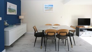 A dining area with a white table, six chairs, a TV, and artwork on the walls. - 2 Lon Y Dryw (Holyhead)