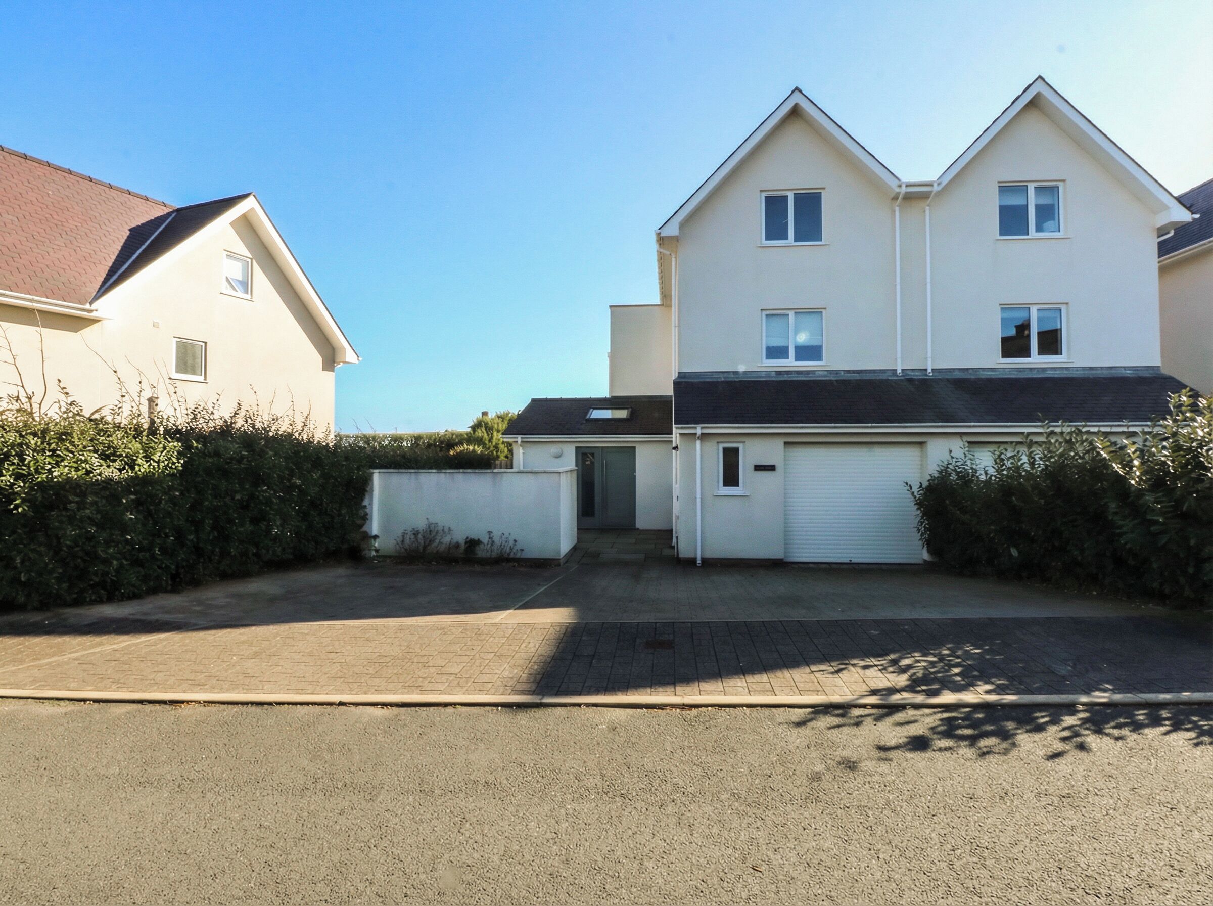 Un immeuble résidentiel à deux étages, doté d’un garage, d’une allée et d’une haie bien entretenue.