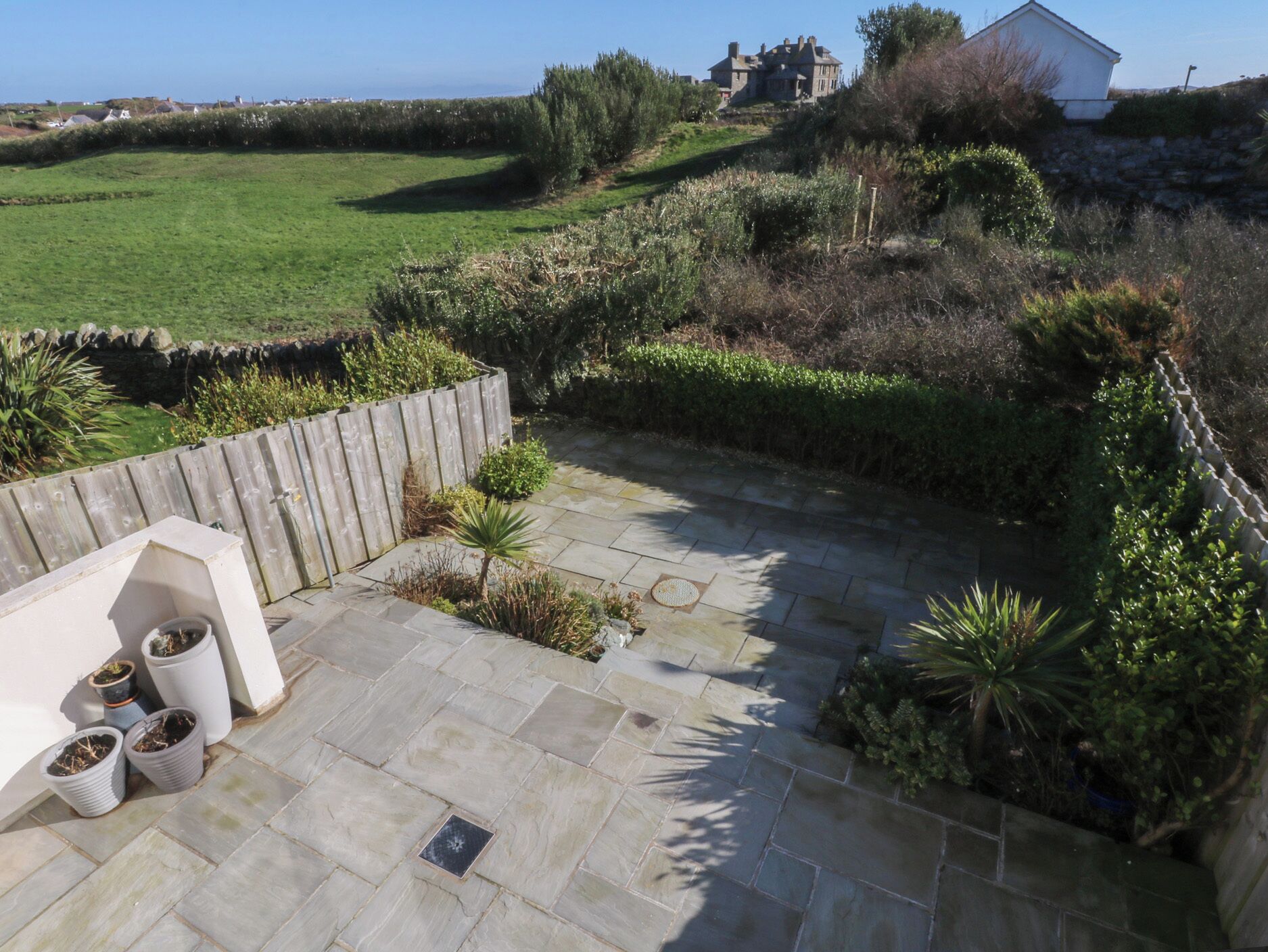 A patio with stone flooring, a wooden fence, and various potted plants.