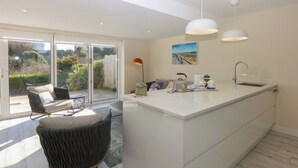 A modern kitchen with a large island, a dining area with a chair, and a view of the garden through the sliding doors. - 2 Lon Y Dryw (Holyhead)