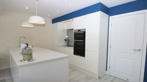 A modern kitchen with white cabinets, a built-in oven, and pendant lighting. - 2 Lon Y Dryw (Holyhead)