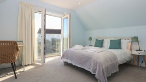 A bedroom with a bed, bedside tables, a chair, and a large window. - 2 Lon Y Dryw (Holyhead)