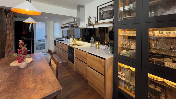 A modern kitchen with a central island, wooden cabinetry, and a dining area with a wooden table and chairs. - Bohemian Beach Cottage (Bournemouth)