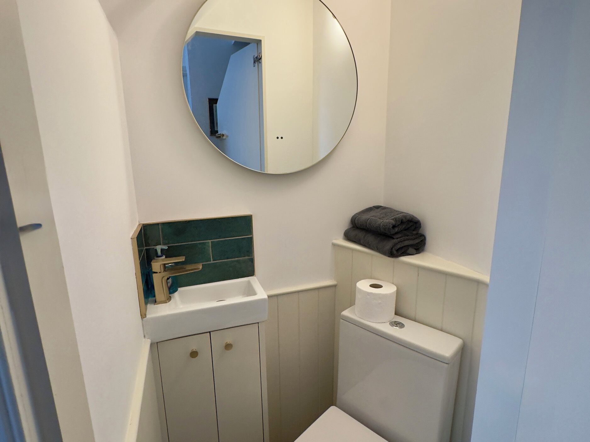 A small bathroom with a white sink, a mirror, a toilet, and a towel shelf.