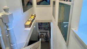 A staircase with a white balustrade, a row of books on a shelf, and a framed artwork above. - Bohemian Beach Cottage (Bournemouth)