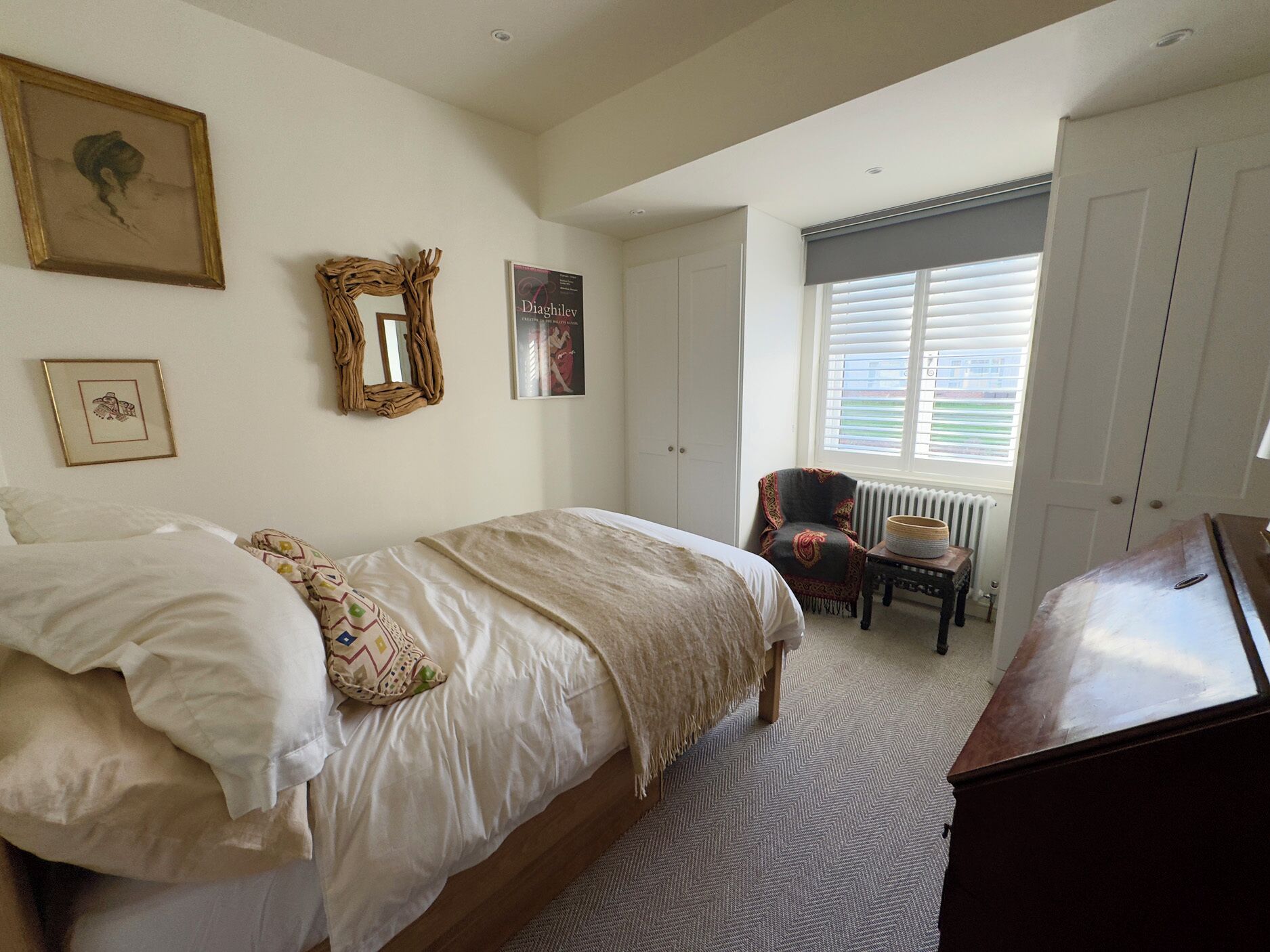 A bedroom with a bed, a chair, a dresser, and a radiator.