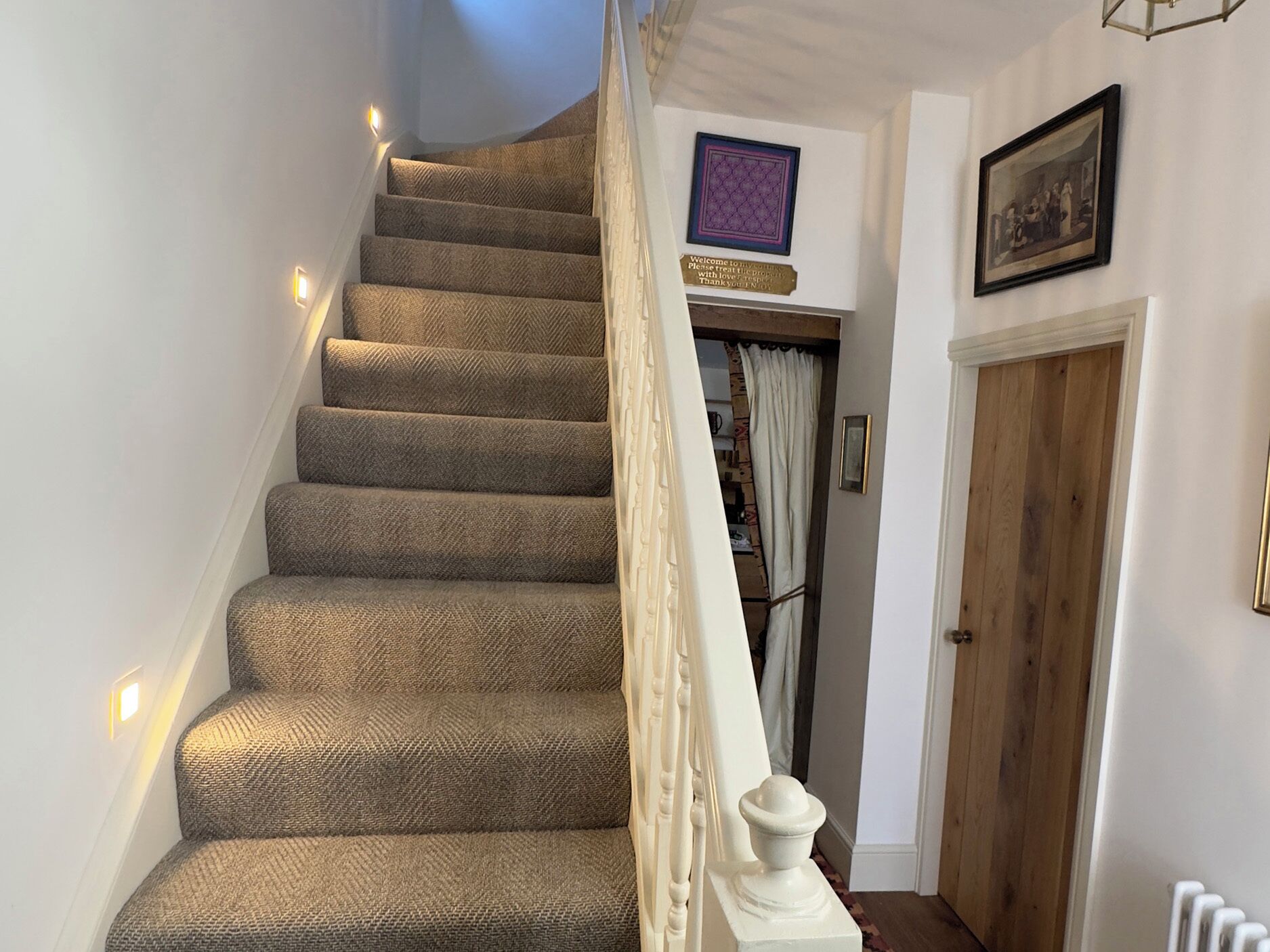 A carpeted staircase with a white balustrade, a door with a wooden panel, and a framed picture on the wall.
