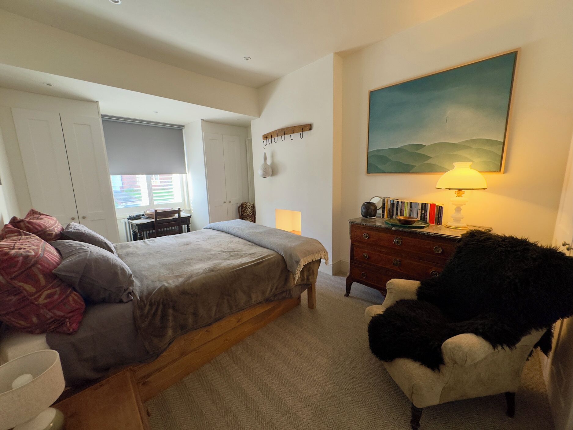 Un dormitorio con cama, cómoda, silla, un cuadro y una lámpara.