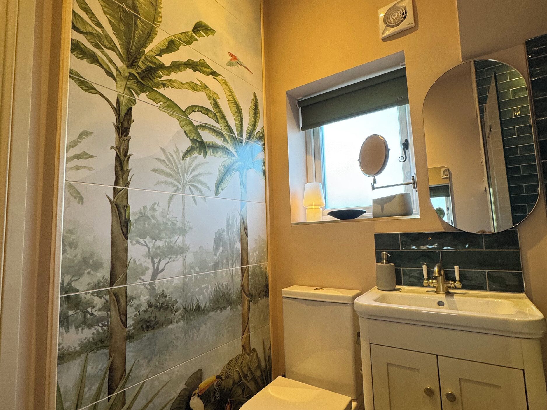 A bathroom with a toilet, sink, and mirror. There is a window with a view of the outside.