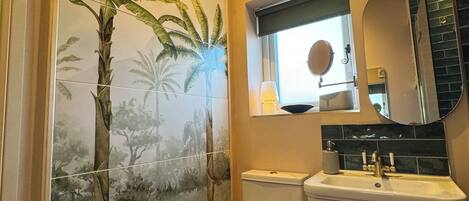 A bathroom with a toilet, sink, and mirror. There is a window with a view of the outside.