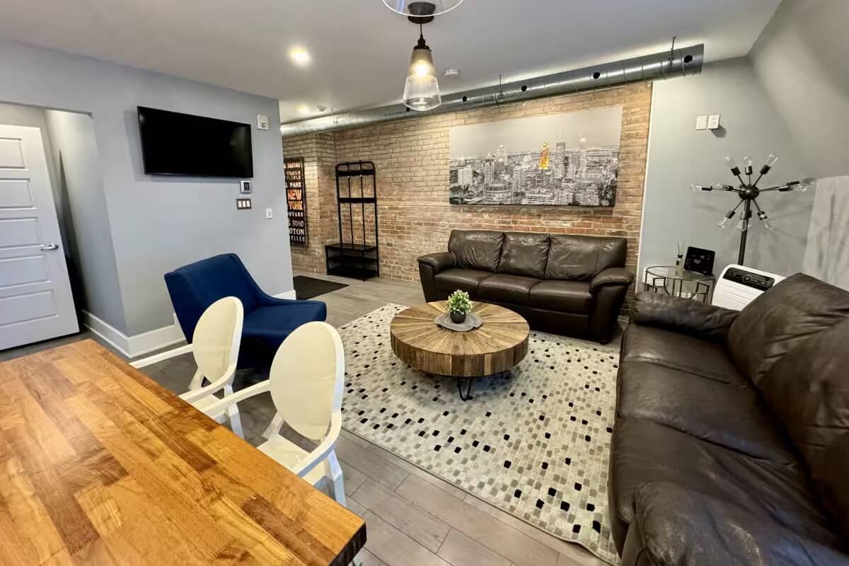 Uma sala de estar moderna com um sofá de couro marrom, uma mesa de centro redonda e uma poltrona azul.