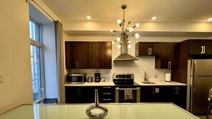 A modern kitchen with dark wooden cabinets, stainless steel appliances, and a glass dining table. - AirStay-Bishop (Montréal)