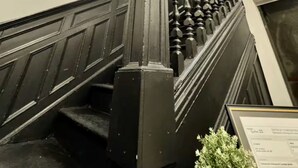A staircase with a black balustrade and a decorative column, leading to a room with a large window and a hanging light fixture. - AirStay-Bishop (Montréal)