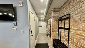 A hallway with a television, a door, a bench, and a brick wall. - AirStay-Bishop (Montréal)