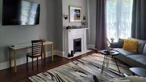 Una sala de estar con chimenea, un televisor de pantalla plana montado en la pared, un sofá con un cojín amarillo y una alfombra estampada.