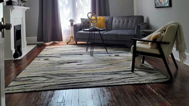 Una sala de estar con un sofá gris, un tapete estampado, una chimenea y un cuadro en la pared.