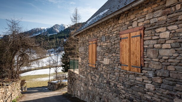 A stone building with wooden shutters, a stone wall, and a view of snow-covered mountains. - Mountain House for 9 Guests (Saint-Lary Soulan)