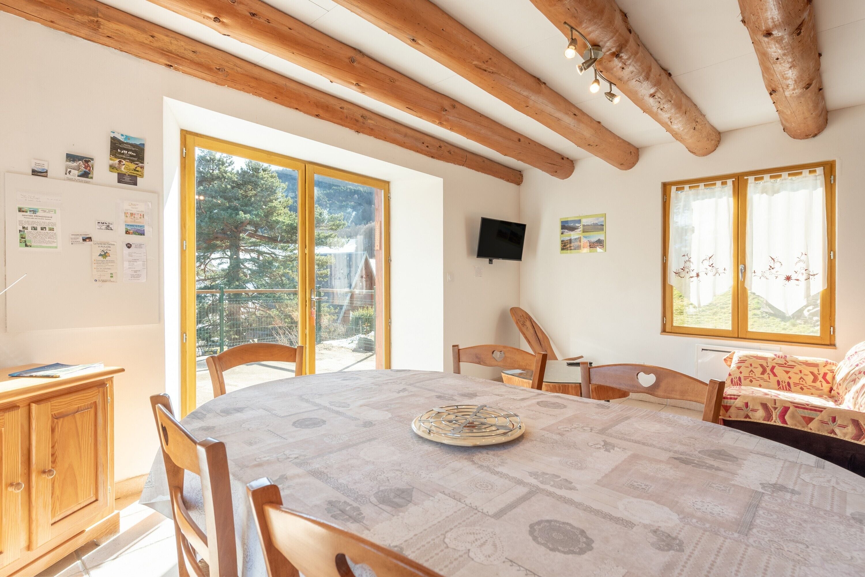 Ein Essbereich mit einem runden Tisch, Holzsesseln, einem Schrank und einem Fernseher an der Wand.