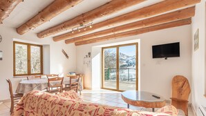 A room with a bed, a dining table, chairs, a TV, and a large window with a view of mountains. - Mountain House for 9 Guests (Saint-Lary Soulan)
