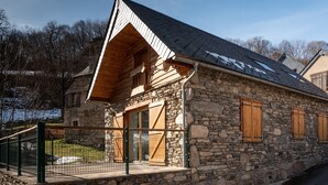 A stone building with a sloped roof, wooden shutters, and a fenced porch. - Mountain House for 9 Guests (Saint-Lary Soulan)