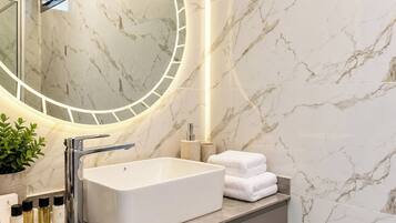 Un baño moderno con un espejo grande, un lavabo rectangular y una encimera con artículos de aseo.