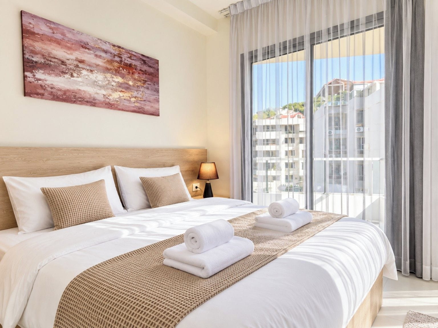 Een hotelkamer met een groot bed, uitzicht op gebouwen door het raam en een schilderij aan de muur.