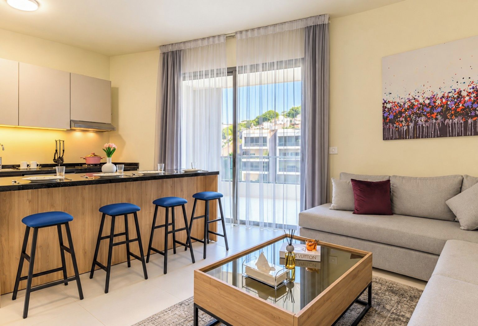 Un salon moderne avec un canapé, une table basse et un coin cuisine équipé d’un tabouret de bar.