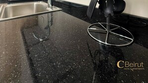 Una cocina moderna con un lavamanos de acero inoxidable, encimera de granito negro y un colgador para utensilios.