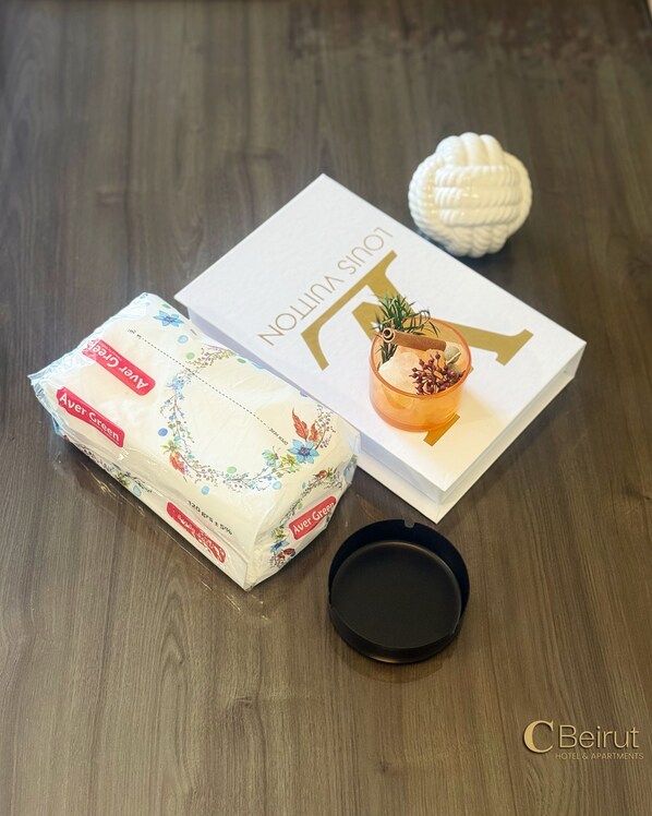 A package of Avera Green toilet paper, a book titled "Louis Vuitton," and a small decorative item on a wooden table. - C Beirut Hotel & Appartment (Mar Roukouz)