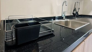 Una cocina con encimera negra, pileta de acero inoxidable y escurridor negro.