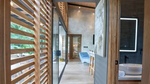 Un pasillo moderno con listones de madera, una puerta de cristal y un baño con lavabo y espejo.