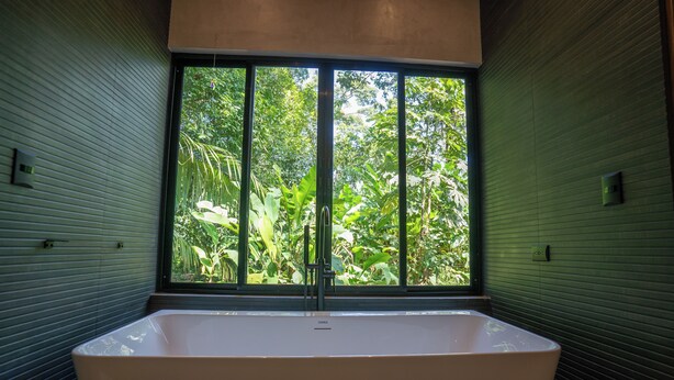 A modern bathroom with a freestanding bathtub, large window, and green sliding doors. - Villa Asencia (Punta Uva)