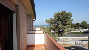 Un balcón con vista al mar, un árbol y un estacionamiento.