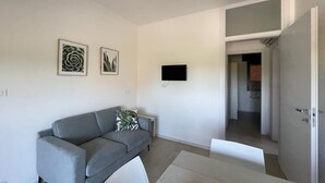 Una sala de estar moderna con un sofá gris, un televisor de pantalla plana montado en la pared y una puerta que da a otra habitación.