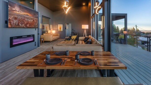 Een moderne eetruimte met een houten tafel gedekt voor vier personen, een bank en een grote televisiescherm.