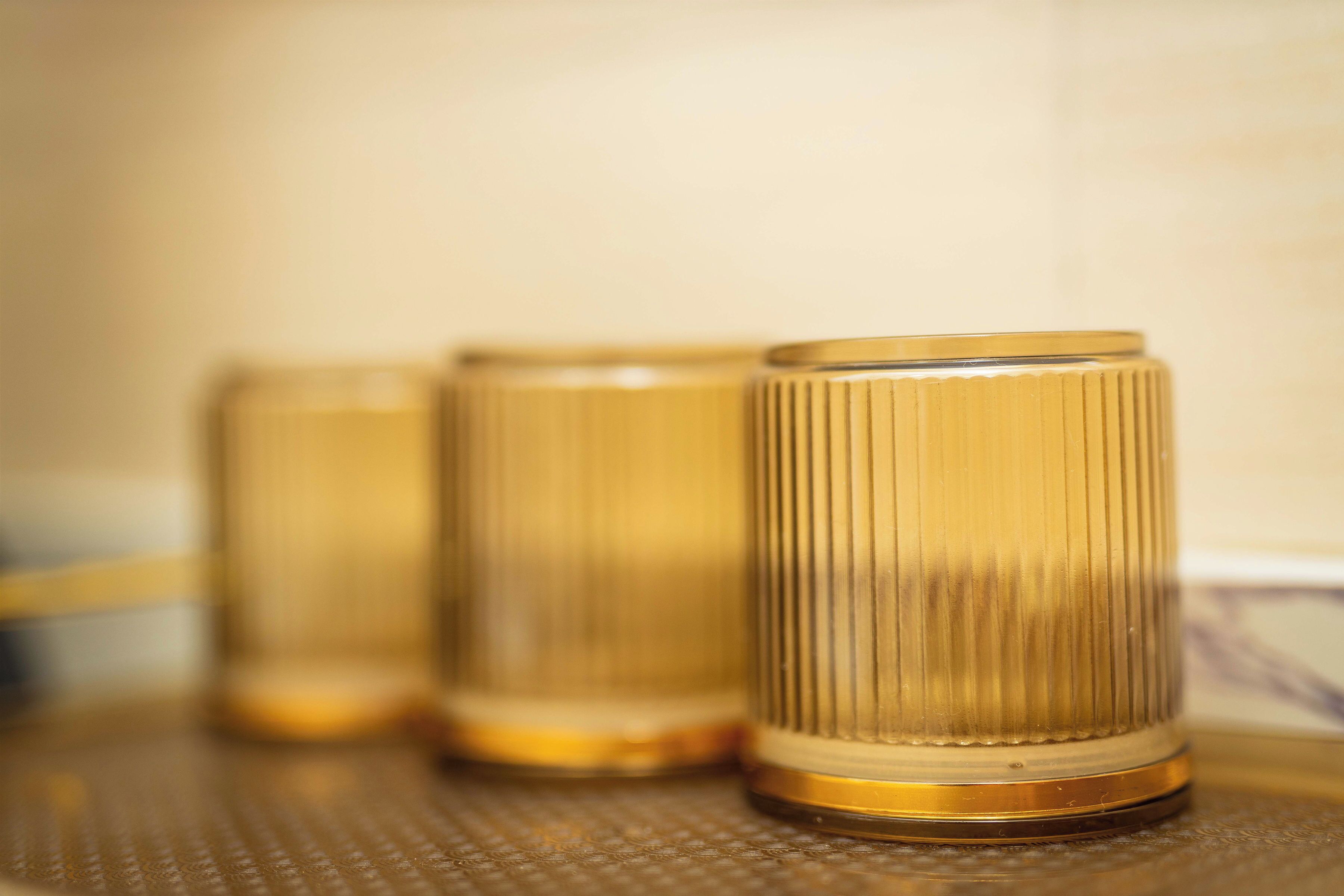 Three glass tumblers with a ribbed texture and a golden rim, placed on a textured surface.