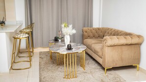A living room with a beige sofa, a round coffee table, and two gold metal chairs. - Libi Apartment-BlueWaters Property  (Accra)
