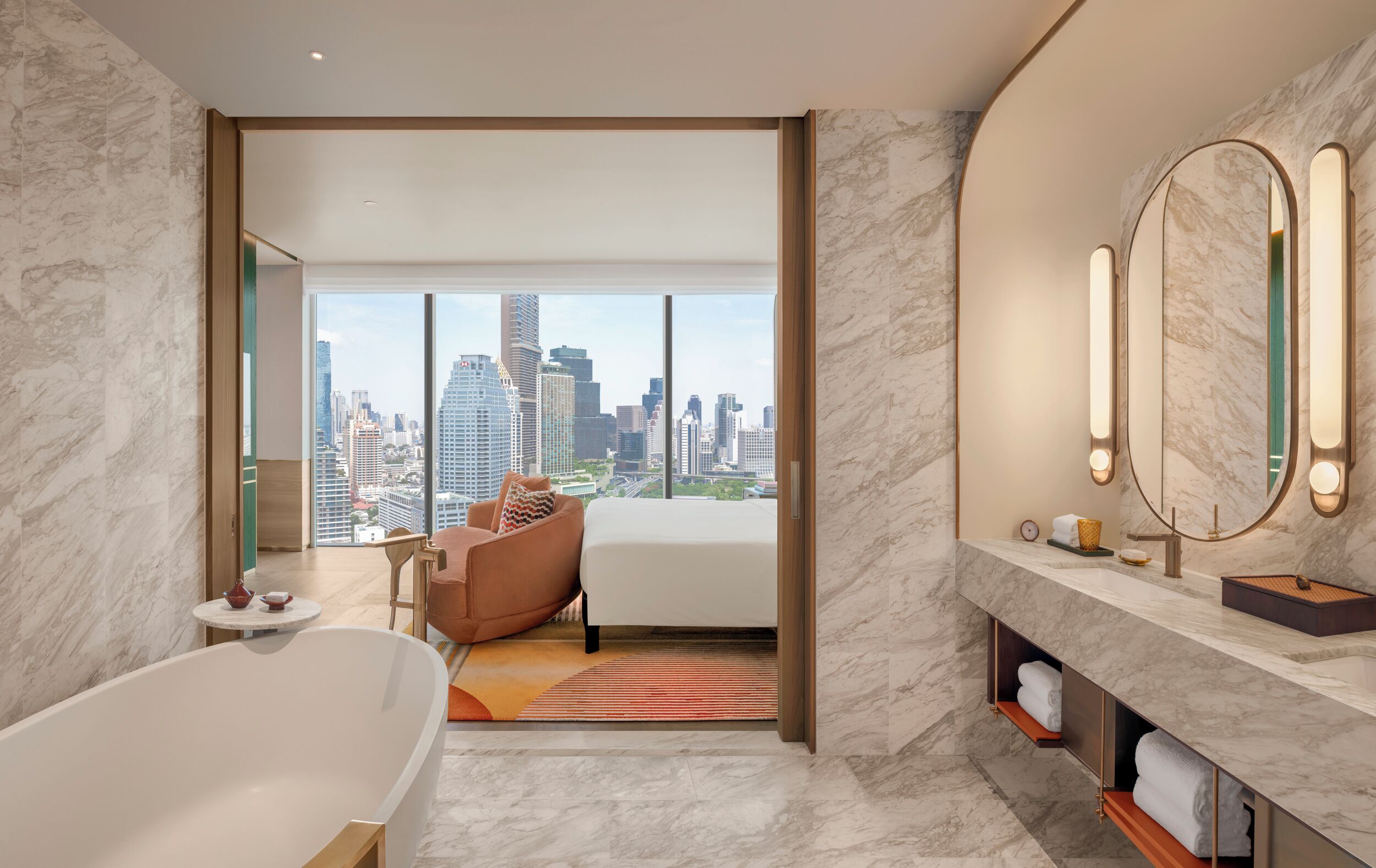 Habitación de hotel moderna con vista a la ciudad, una bañera grande, un sofá y un tocador con espejo.