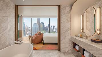 Habitación de hotel moderna con vista a la ciudad, una bañera grande, un sofá y un tocador con espejo.