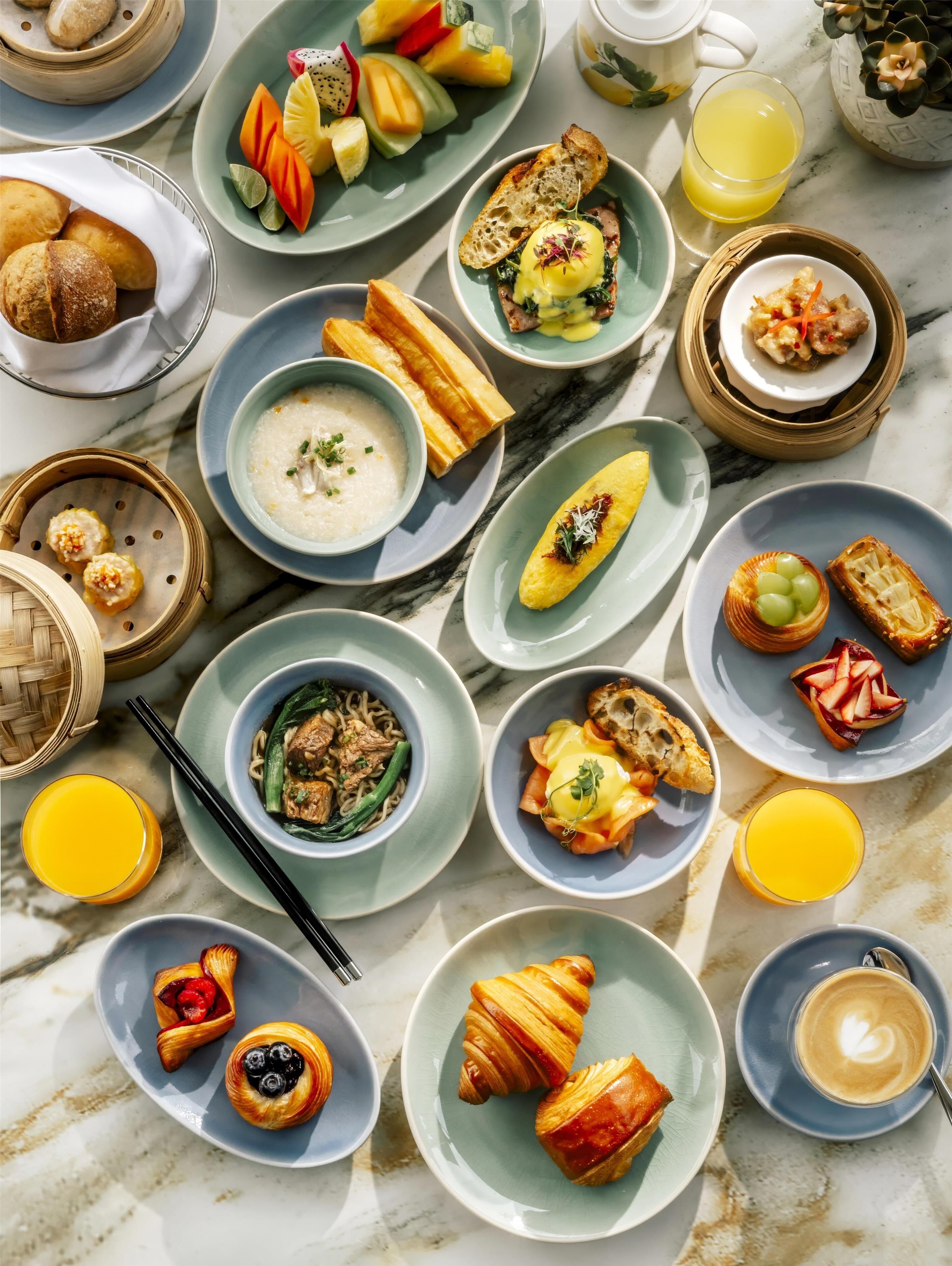 A variety of dishes and drinks on a marble table, including bread, soup, and fruit.
