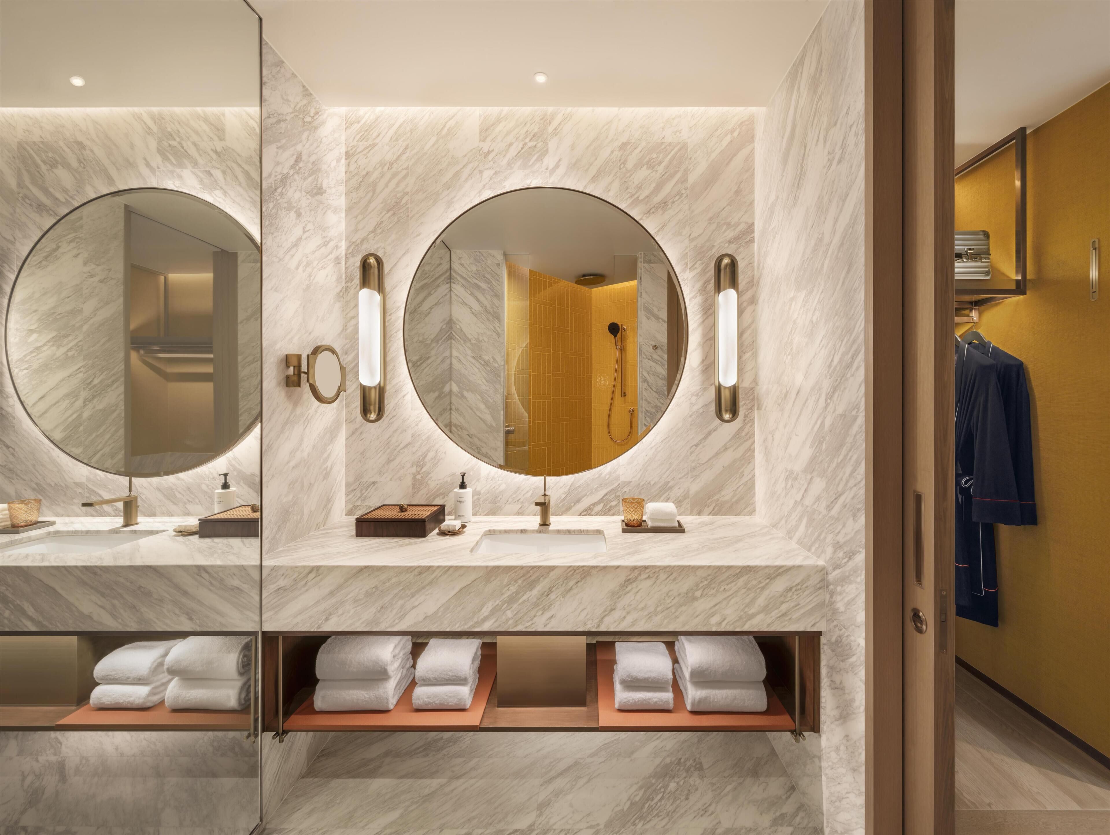 A modern bathroom with marble walls, two large mirrors, a shower, and a towel rack.