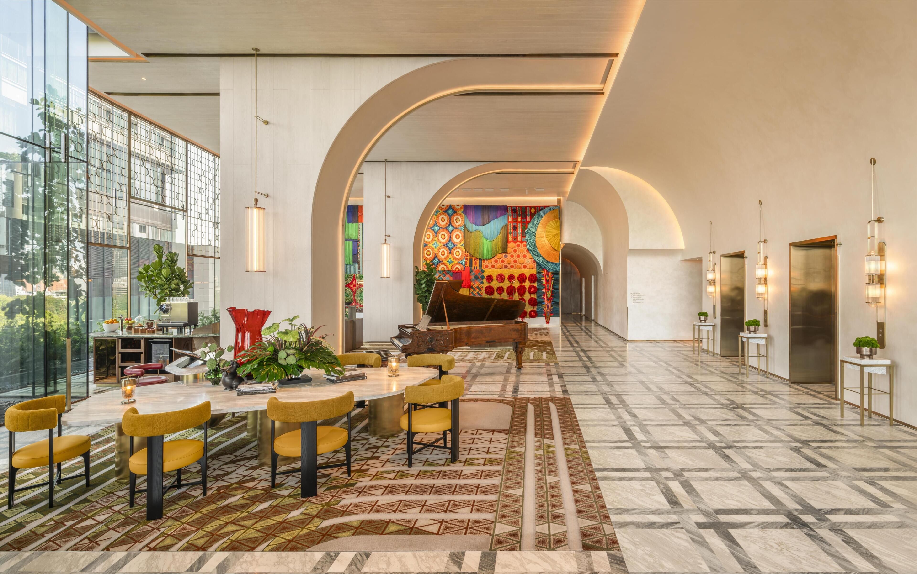 A spacious lobby with a grand piano, a dining area with yellow chairs, and a colorful mural in the background.