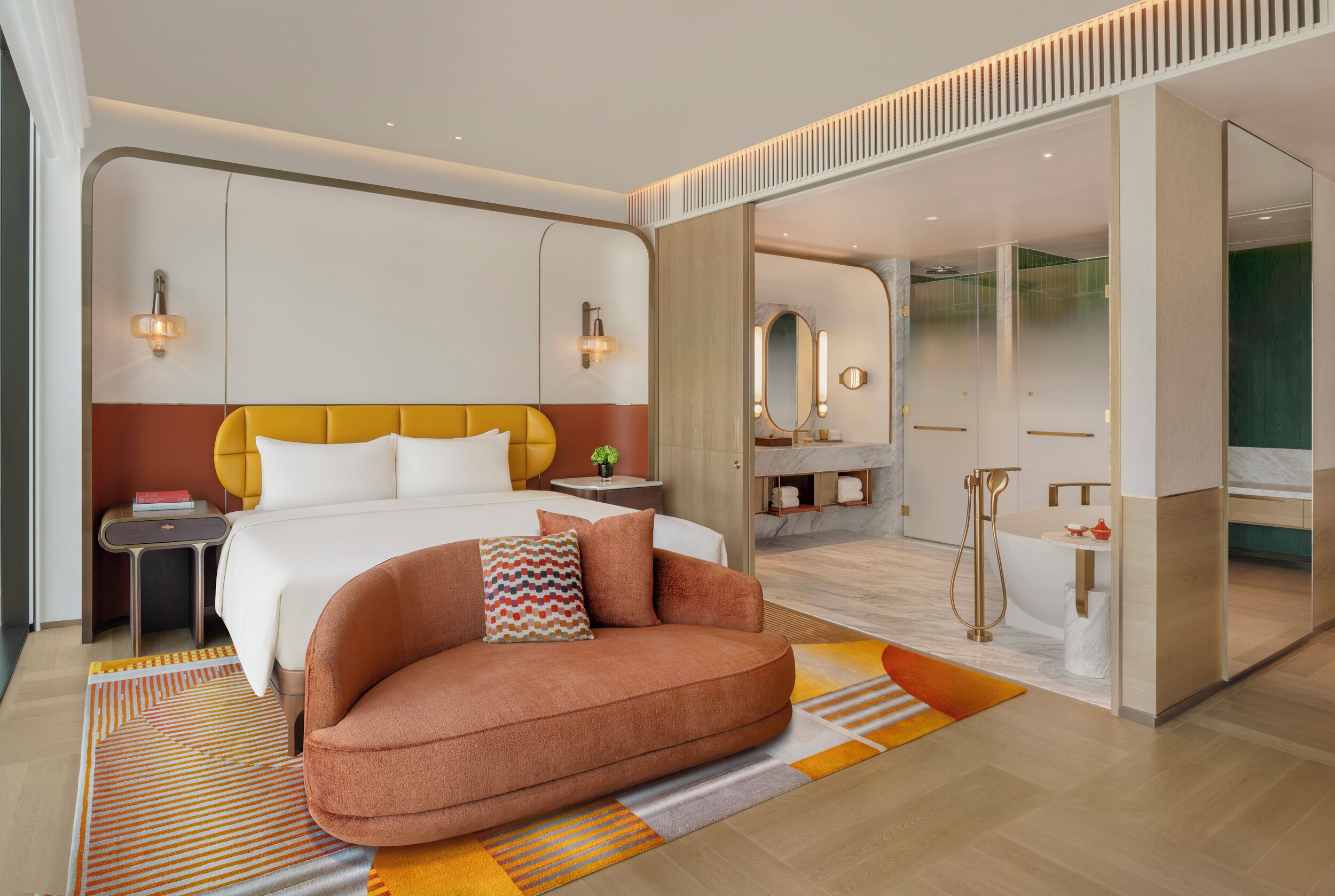 Una habitación de hotel moderna con una cama grande, un sofá, un baño con bañera y un espejo.
