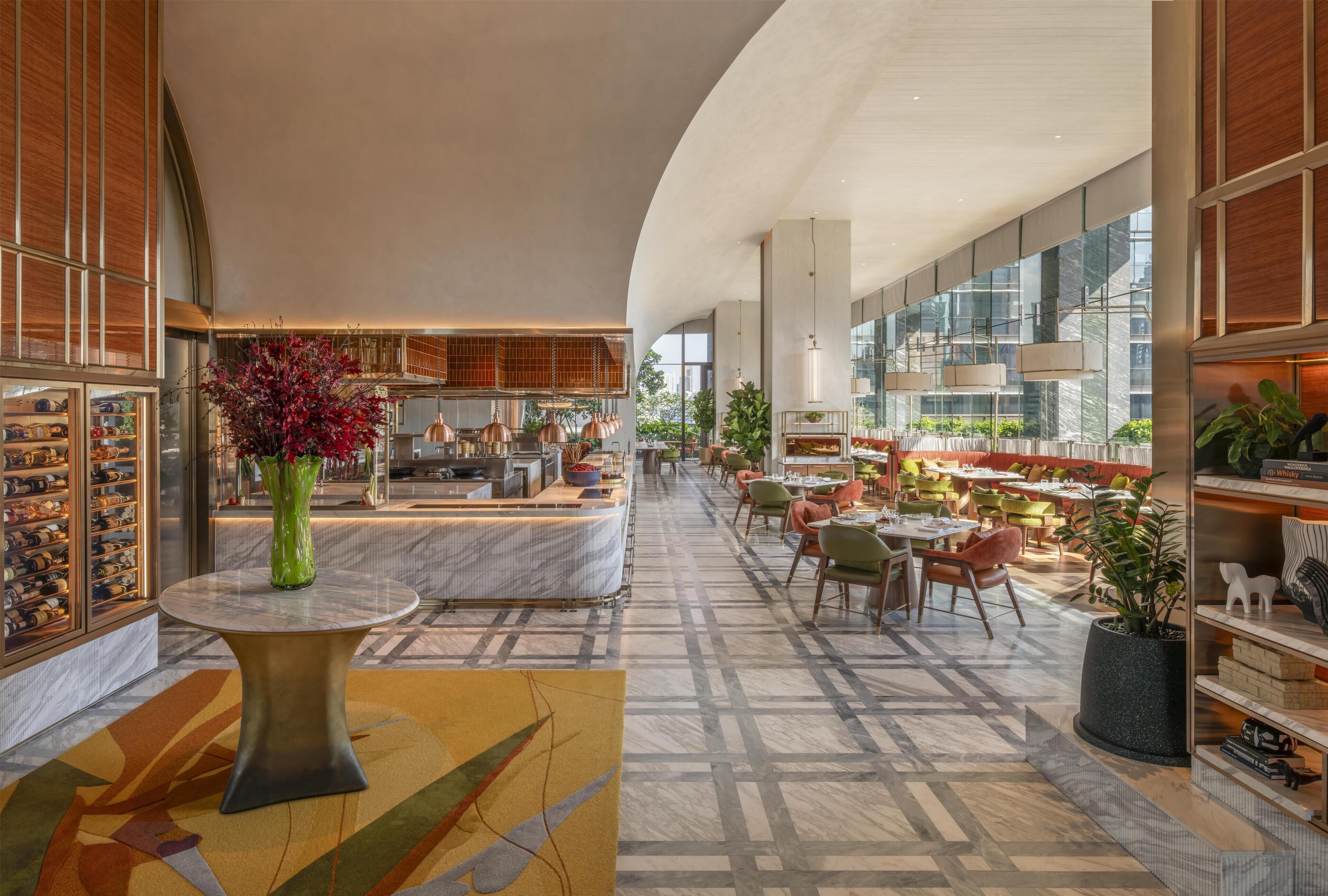 A spacious hotel lobby with a marble reception desk, seating area, and large windows offering views of the city.