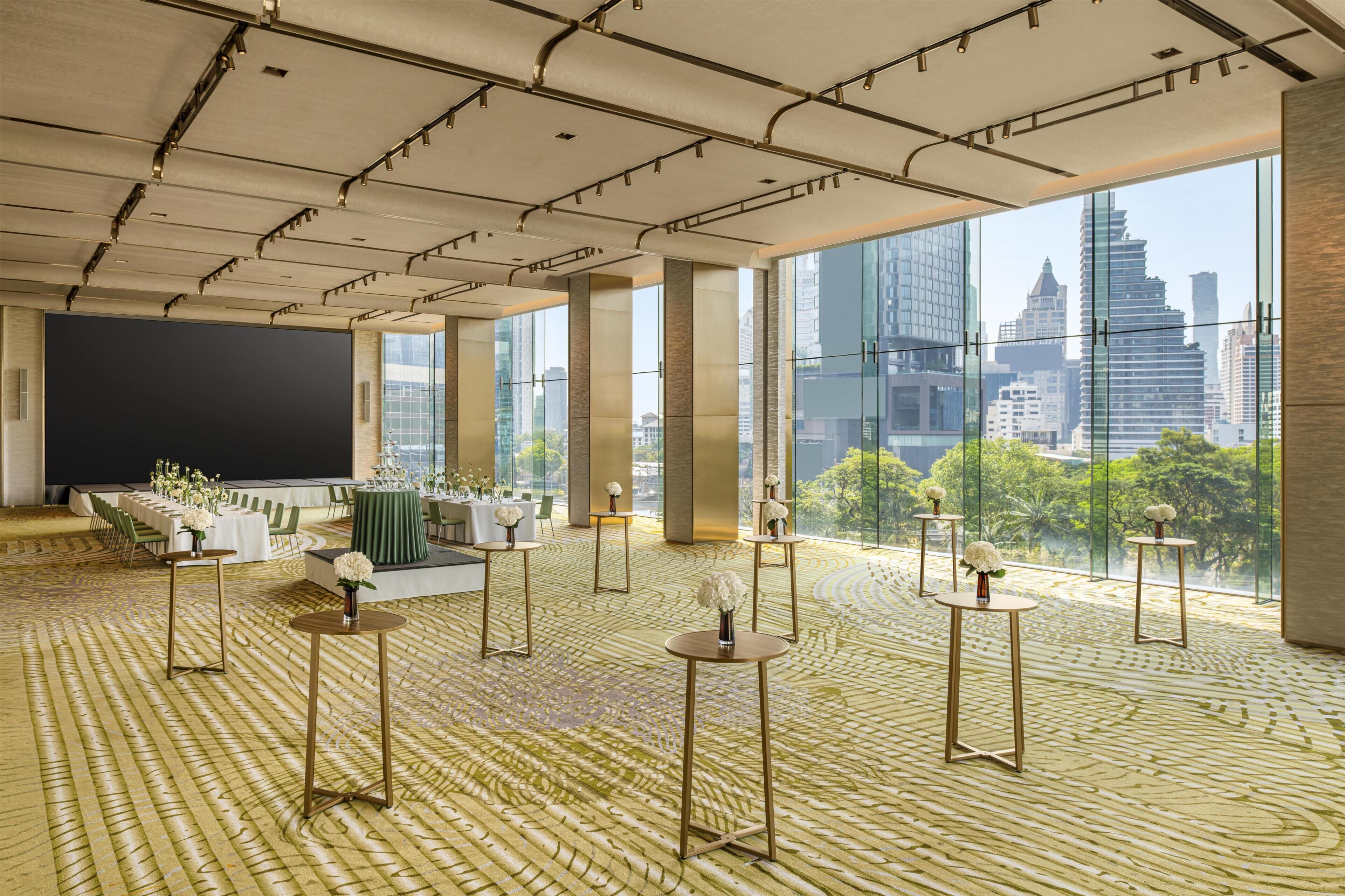 Een ruime hotellobby met grote ramen, een podium en tafels met bloemdecoraties.